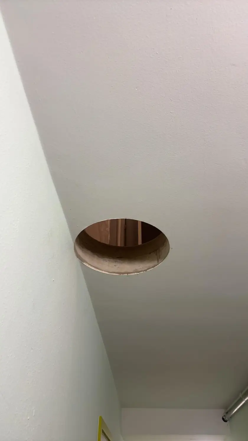 Ouverture circulaire dans un plafond peint, le pourtour de la découpe est intact.
