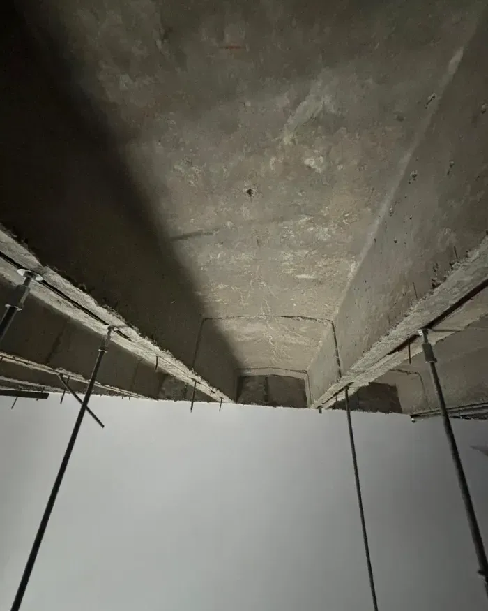 Plafond en béton en grande hauteur, vu du dessous entre des tiges de suspension.