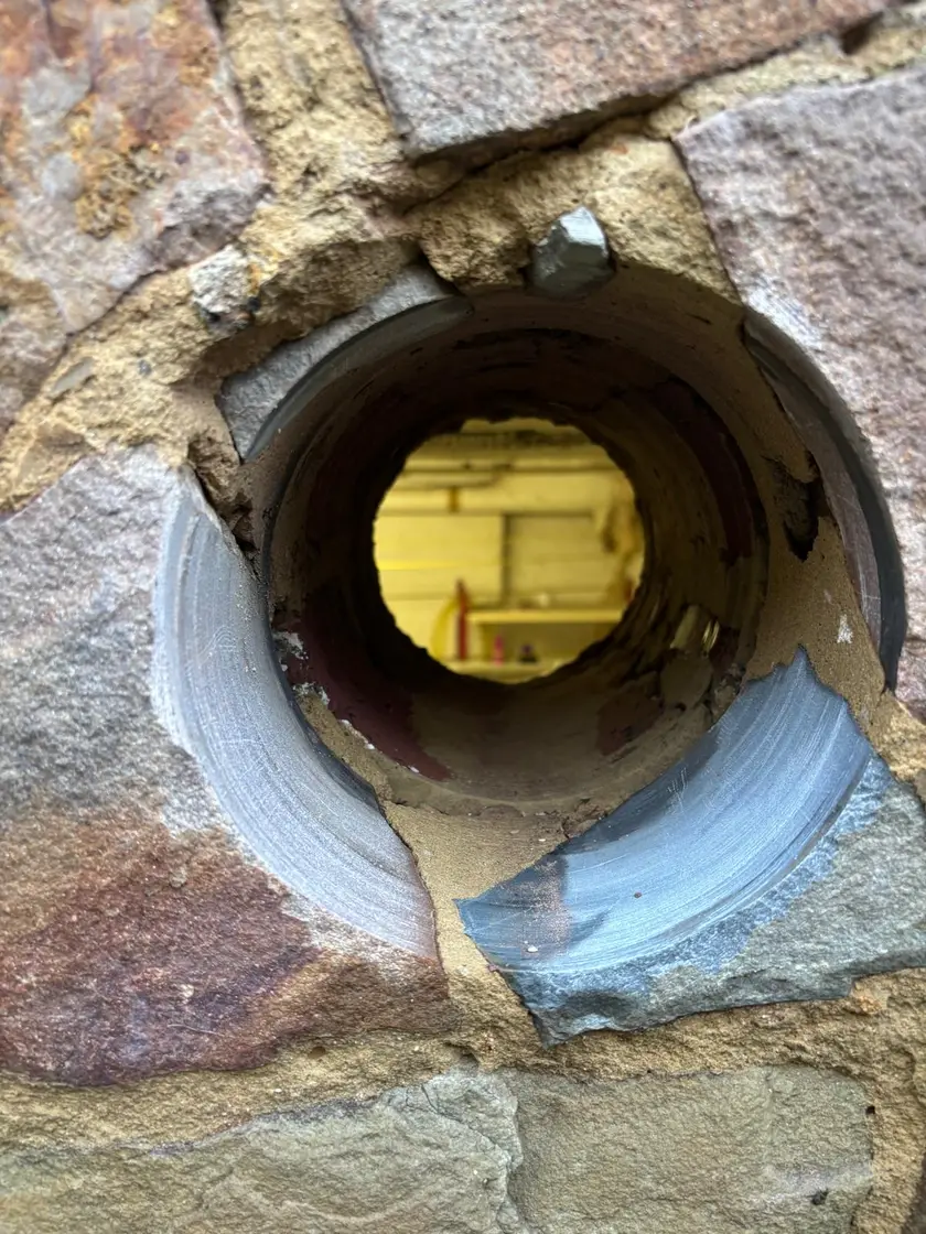 Vue rapprochée dans un carottage traversant un mur de pierre : le conduit est net sur toute sa longueur et laisse voir la pièce éclairée de l’autre côté.