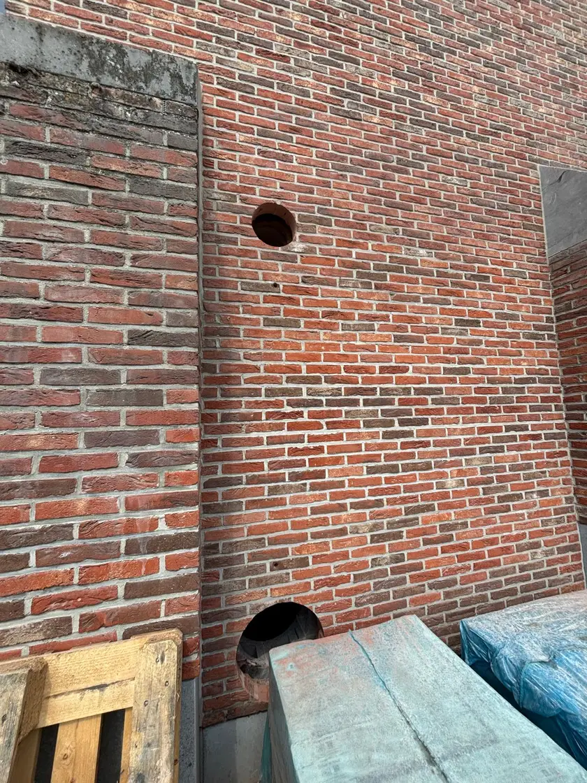 Deux percements circulaires de diamètres différents dans une façade de brique neuve.